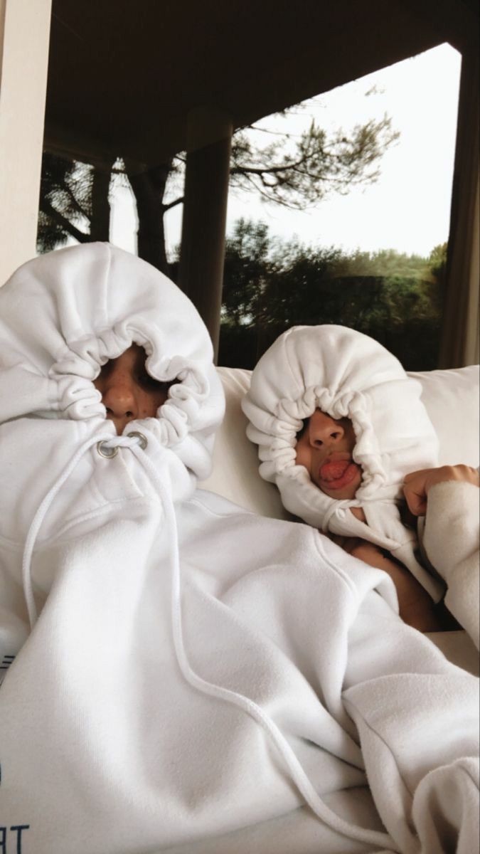 Two people bundled into white hoodies on a couch
